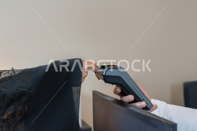 Development of technology and technology, the possibility of paying bills using electronic cards, a close-up image of the hand of an Arab Gulf Emirati woman wearing a black abaya paying at the cashier using a bank credit card, the use of modern advanced means and technologies, facilitating the buying and selling processes