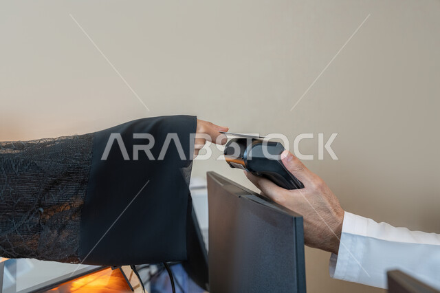 Facilitating buying and selling operations, using modern advanced means and technologies, the possibility of paying bills using electronic cards, the development of technology and technology, a close-up image of the hand of an Arab Gulf Emirati woman wearing a black abaya paying at the cashier using a bank credit card