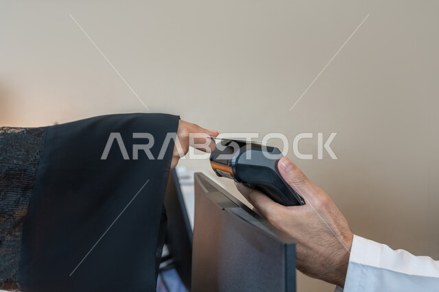 Using modern advanced means and technologies, the possibility of paying bills using electronic cards, the development of technology and technology, a close-up image of the hand of an Arab Gulf Emirati woman wearing a black abaya paying at the cashier using a bank credit card, facilitating the purchase and sale processes