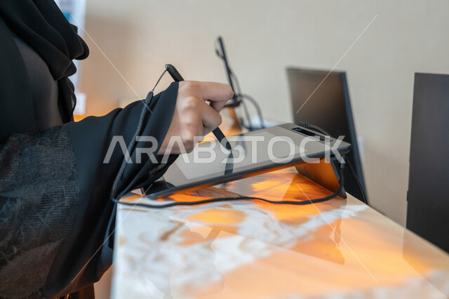 Using modern advanced means and techniques in daily life, development of technology and technology, close-up image of the hand of an Arab Gulf Emirati woman wearing a black abaya holding a pen in her hand tapping on the screen of a tablet