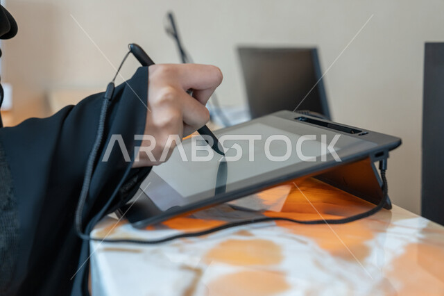 تطور التقنية والتكنولوجيا، صورة مقربة ليد امرأة عربية خليجية اماراتية ترتدي العباءة السوداء تحمل بيدها قلم تقوم بالنقر على شاشة جهاز التابلت، استخدام الوسائل والتقنيات الحديثة المتطورة في الحياة اليومية