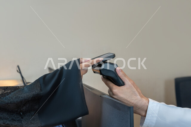 Development of technology and technology, ease of buying and selling process, close-up of the hand of an Arab Gulf Emirati woman paying the bill via mobile phone at the cashier, use of modern means and technologies in electronic payment, customer service for inquiries and questions