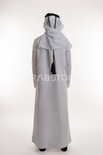 The concept of masculinity and strength, elegance and interest in external appearance, portrait from the back of an Arab Gulf Emirati man wearing the Emirati kandura and ghutra, standing straight and looking at something, full-length body image, white background