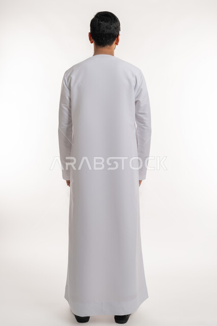 الأناقة والاهتمام بالمظهر الخارجي، بورتريه من الخلف لرجل عربي خليجي إماراتي يرتدي الكندورة الاماراتية يقف باستقامة وينظر إلى شي ما، مفهوم الرجولة والقوة، صورة الجسم بالطول الكامل، خلفية بيضاء