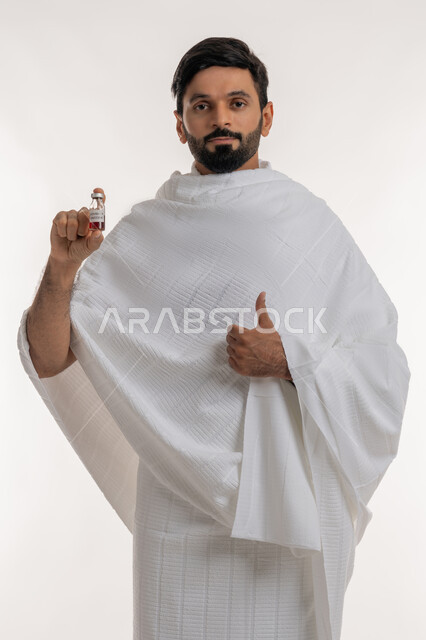 النظر إلى الكاميرا بإيماءات علامة الجودة والامتياز، أداء مناسك الحج والعمرة، تلقي التطعيم ضد فايروس كورونا، بورتريه لرجل عربي خليجي إماراتي يرتدي ثياب الإحرام يحمل بيده جرعة لقاح كوفيد - 19 يرفع إبهامه إلى الأعلى، اتباع إجراءات وزارة الصحة، خلفية بيضاء