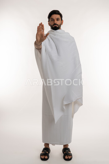 الأمر بالنهي عن فعل شيء ما، أداء مناسك الحج والعمرة، العبادة والتقرب إلى الله، بورتريه لشاب خليجي عربي إماراتي يرتدي ثياب الإحرام يقف باستقامة يرفع كفه للأعلى، طلب عدم التدخل وخفض الصوت، مفهوم أركان الإسلام والفرائض الدينية، الجسم بالطول الكامل، خلفية بيضاء