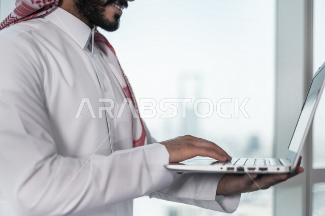 رجل اعمال عربي خليجي سعودي يستخدم جهاز الحاسوب المحمول ، العمل عن بعد ، انجاز مهام العمل ،تحقيق اهداف الشركة ، متابعة وتطوير العمل