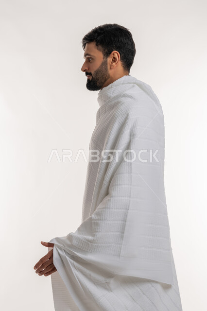 الاستعداد لمصافحة أحد ما، تأدية مناسك الحج والعمرة، بورتريه من الجانب لشاب خليجي عربي إماراتي يرتدي ثياب الإحرام يقف باستقامة ينظر إلى شيء ما، مفهوم أركان الإسلام، العبادة والتقرب إلى الله، أداء الفرائض الدينية، خلفية بيضاء