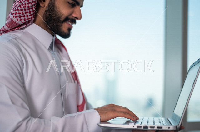 رجل اعمال عربي خليجي سعودي يستخدم جهاز الحاسوب المحمول ، العمل عن بعد ، انجاز مهام العمل ،تحقيق اهداف الشركة ، متابعة وتطوير العمل
