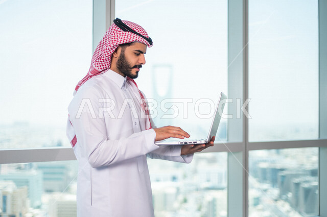 رجل اعمال عربي خليجي سعودي يستخدم جهاز الحاسوب المحمول ، العمل عن بعد ، انجاز مهام العمل ،تحقيق اهداف الشركة ، متابعة وتطوير العمل