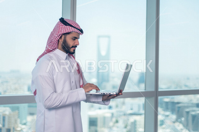 رجل اعمال عربي خليجي سعودي يستخدم جهاز الحاسوب المحمول ، العمل عن بعد ، انجاز مهام العمل ،تحقيق اهداف الشركة ، متابعة وتطوير العمل