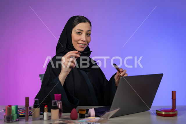لشغف بوضع المكياج, مفهوم الإهتمام بالجمال والبشرة، التسويق لمنتجات ومستحضرات الميكآب في المتاجر و عبر الإنترنت، خبيرة تجميل عربية خليجية اماراتية محجبة ترتدي العباءة السوداء تحمل بيدها قلم المسكرة وتنظر إلى الكاميرا، شابة سعودية تهتم بجمالها
