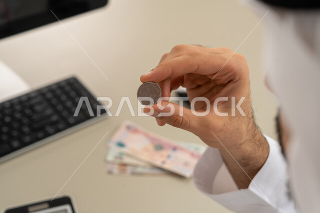 عرض الإصدار الجديد للنقود الاماراتية، العملة المتداولة في أسواق الامارات العربية المتحدة،  بورتريه لرجل عربي خليجي اماراتي يرتدي الكندورة والغترة يمسك بيده الفلوس، الأعمال الاقتصادية المالية، محاولة إدارة المصروف المنزلي بتدبر، السعي نحو الادخار، خلفية بيضاء
