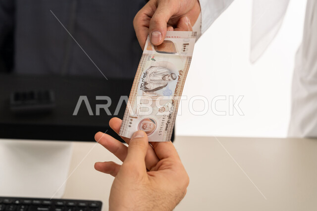 Recording customer payments on laptop, currency in UAE markets, portrait of an Emirati Gulf Arab man wearing a white kandura and ghutra paying bills and purchase accounts, using modern and advanced technical devices, white background