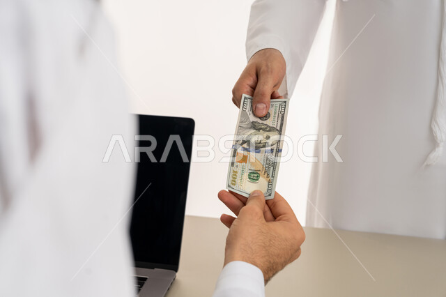 تسجيل تسديدات العملاء على جهاز الحاسوب المحمول، العملة المتداولة في أسواق الامارات العربية المتحدة،  بورتريه لرجل عربي خليجي اماراتي يرتدي الكندورة والغترة البيضاء يقوم بدفع الفواتير وحسابات المشتريات، استخدام الاجهزة التقنية الحديثة والمتطورة، خلفية بيضاء