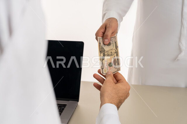 تسجيل تسديدات العملاء على جهاز الحاسوب المحمول، العملة المتداولة في أسواق الامارات العربية المتحدة،  بورتريه لرجل عربي خليجي اماراتي يرتدي الكندورة والغترة البيضاء يقوم بدفع الفواتير وحسابات المشتريات، استخدام الاجهزة التقنية الحديثة والمتطورة، خلفية بيضاء