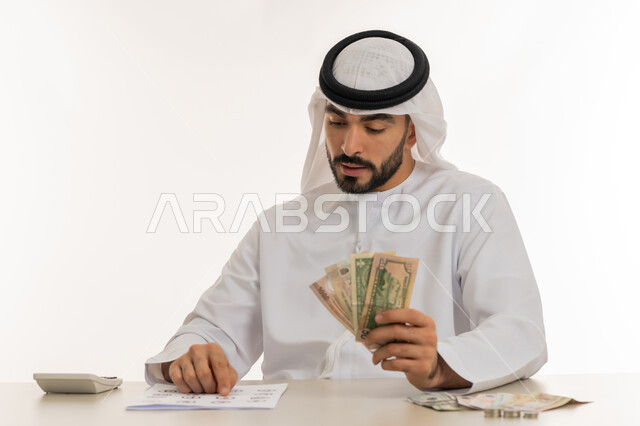 عرض الإصدار الجديد للنقود الاماراتية، العملة المتداولة في أسواق الامارات العربية المتحدة،  بورتريه لرجل عربي خليجي اماراتي يرتدي الكندورة والغترة يمسك بيده الفلوس، الأعمال الاقتصادية المالية، محاولة إدارة المصروف المنزلي بتدبر، السعي نحو الادخار، خلفية بيضاء