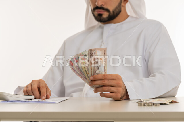عرض الإصدار الجديد للنقود الاماراتية، العملة المتداولة في أسواق الامارات العربية المتحدة،  بورتريه لرجل عربي خليجي اماراتي يرتدي الكندورة والغترة يمسك بيده الفلوس، الأعمال الاقتصادية المالية، محاولة إدارة المصروف المنزلي بتدبر، السعي نحو الادخار، خلفية بيضاء