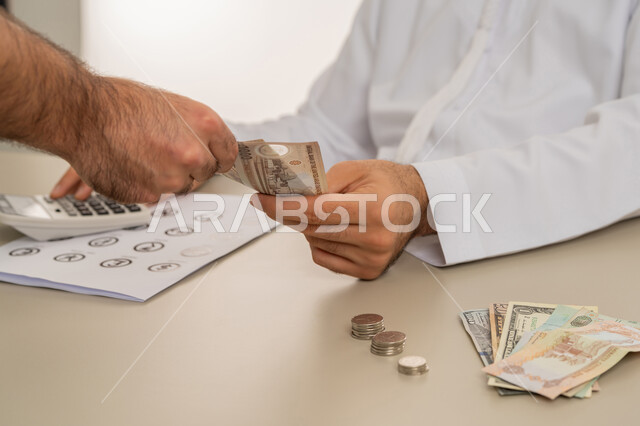 مفهوم الدفع نقدا، عملية تسديد النقود بواسطة الدراهم، استلام وتسليم الأمانات، العملة المتداولة في أسواق الامارات العربية المتحدة، الأعمال الاقتصادية المالية، بورتريه مقرب لرجل عربي خليجي اماراتي يرتدي الكندورة يقوم بدفع الفواتير وحسابات المشتريات، خلفية بيضاء