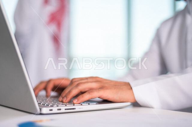 رجل اعمال عربي خليجي سعودي يستخدم جهاز الحاسوب المحمول ، العمل عن بعد ، انجاز مهام العمل ،تحقيق اهداف الشركة ، متابعة وتطوير العمل
