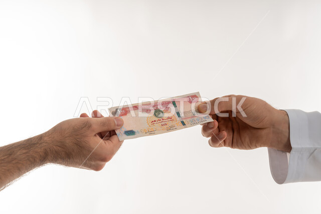 مفهوم الدفع نقدا، عملية تسديد النقود بواسطة الدراهم، استلام وتسليم الأمانات، العملة المتداولة في أسواق الامارات العربية المتحدة، الأعمال الاقتصادية المالية، بورتريه مقرب لرجل عربي خليجي اماراتي يرتدي الكندورة يقوم بدفع الفواتير وحسابات المشتريات، خلفية بيضاء