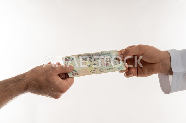 مفهوم الدفع نقدا، عملية تسديد النقود بواسطة الدراهم، استلام وتسليم الأمانات، العملة المتداولة في أسواق الامارات العربية المتحدة، الأعمال الاقتصادية المالية، بورتريه مقرب لرجل عربي خليجي اماراتي يرتدي الكندورة يقوم بدفع الفواتير وحسابات المشتريات، خلفية بيضاء