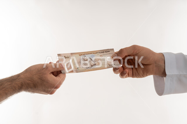 مفهوم الدفع نقدا، عملية تسديد النقود بواسطة الدراهم، استلام وتسليم الأمانات، العملة المتداولة في أسواق الامارات العربية المتحدة، الأعمال الاقتصادية المالية، بورتريه مقرب لرجل عربي خليجي اماراتي يرتدي الكندورة يقوم بدفع الفواتير وحسابات المشتريات، خلفية بيضاء