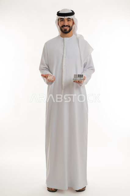 النظر الى الكاميرا بايماءات الثقة بالنفس ، الأعمال الاقتصادية المالية، محاولة إدارة المصروف المنزلي بتدبر، بورتريه لرجل عربي خليجي اماراتي يرتدي الكندورة والغترة يمسك بإحدى يديه الحاسبة الرقمية وباليد الأخرى مجموعة من النقود، السعي نحو التوفير والادخار، خلفية بيضاء