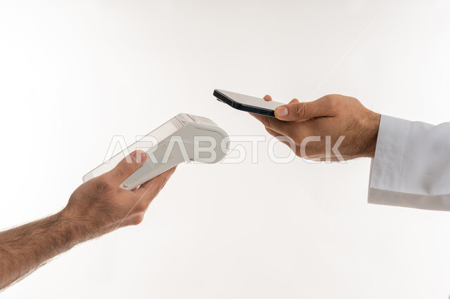 استخدام الوسائل والتقنيات الحديثة المتطورة، إمكانية تسديد الفواتير عن طريق جهاز الدفع الالكتروني، بورتريه ليد رجل عربي خليجي اماراتي يرتدي الكندورة يسدد عند أمين الصندوق باستخدام جهاز الهاتف المحمول، تسهيل عمليات الشراء والبيع، خلفية بيضاء