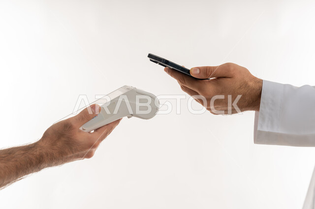 استخدام الوسائل والتقنيات الحديثة المتطورة، إمكانية تسديد الفواتير عن طريق جهاز الدفع الالكتروني، بورتريه ليد رجل عربي خليجي اماراتي يرتدي الكندورة يسدد عند أمين الصندوق باستخدام جهاز الهاتف المحمول، تسهيل عمليات الشراء والبيع، خلفية بيضاء