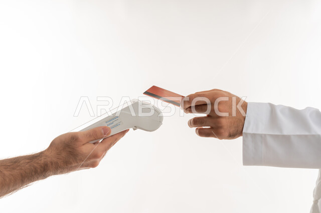 امكانية تسديد الفواتيرعن طريق البطافات الالكترونية، تسهيل عمليات الشراء والبيع، استخدام الوسائل والتقنيات الحديثة المتطورة، بورتريه مقرب ليد رجل عربي خليجي اماراتي يرتدي الكندورة يقوم بالدفع باستخدام بطاقة الإئتمان البنكية، خلفية بيضاء