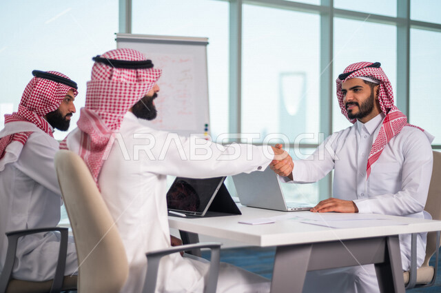 موظفان عربيان خليجيان سعوديان يتصافحان داخل الشركة ، اتفاق عمل بين رجال الاعمال ، صفقة ناجحة ، تعاون تجاري ، عمل جماعي مشترك