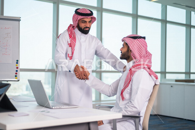 Two Saudi Arabian Gulf men shaking hands inside the company, business agreement between businessmen, successful deal, commercial cooperation, joint team work