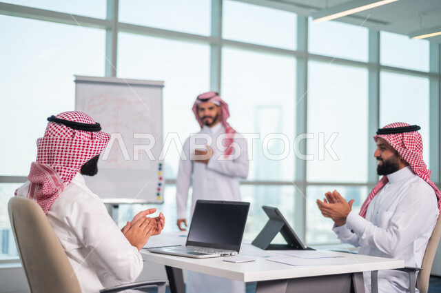 A group of Saudi Gulf businessmen meeting inside the company, using the laptop and tablet during the meeting, listening to the team leader, discussing the company’s goals and policy, explaining the business strategy, discussing a project, a workshop, trai
