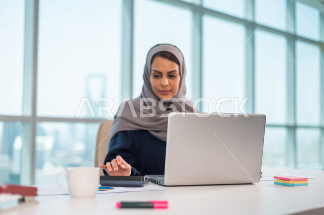 سيدة اعمال عربية خليجية سعودية تستخدم جهاز الحاسوب المحمول ،تستخدم الالة الحاسبة لاجراء العمليات الحسابية والمحاسبية ،  العمل عن بعد ، انجاز مهام العمل ،تحقيق اهداف الشركة ، متابعة وتطوير العمل