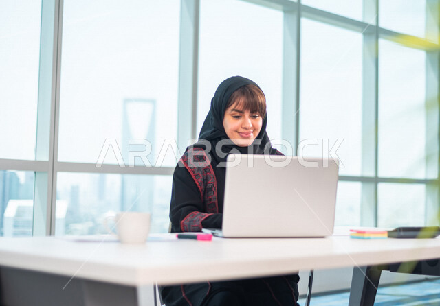 سيدة اعمال عربية خليجية سعودية تستخدم جهاز الحاسوب المحمول ، العمل عن بعد ، انجاز مهام العمل ،تحقيق اهداف الشركة ، متابعة وتطوير العمل