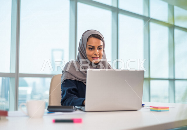 سيدة اعمال عربية خليجية سعودية تستخدم جهاز الحاسوب المحمول ، العمل عن بعد ، انجاز مهام العمل ،تحقيق اهداف الشركة ، متابعة وتطوير العمل