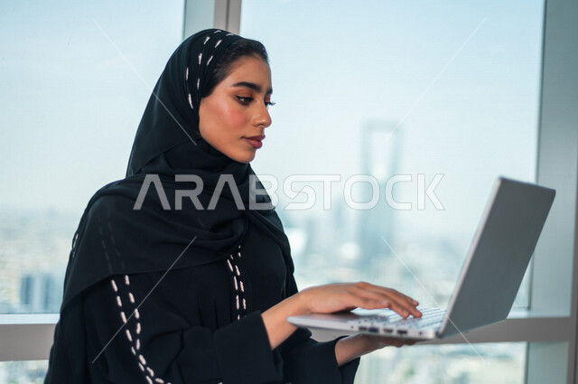 A Saudi Arabian Gulf business woman using a laptop computer, working remotely, completing work tasks, achieving company goals, following up and developing work