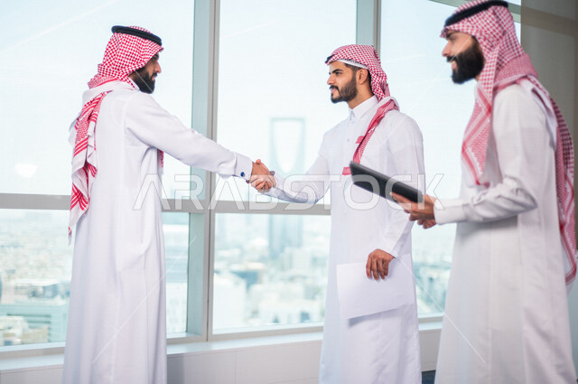 Two Saudi Arabian Gulf men shaking hands inside the company, business agreement between businessmen, successful deal, commercial cooperation, joint team work