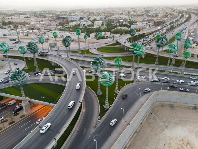 حركة المرور في شوارع وطرقات العاصمة في النهار، الفن الهندسي المعماري للمجسمات الفنية على شكل أشجار خضراء، معالم الرياض المشهورة، دوار عرقة على تقاطع طريق الملك عبد لله مع الملك خالد، تنشيط السياحة في المملكة العربية السعودية