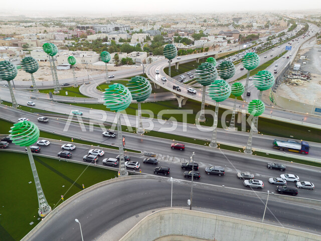 حركة المرور في شوارع وطرقات العاصمة في النهار، الفن الهندسي المعماري للمجسمات الفنية على شكل أشجار خضراء، معالم الرياض المشهورة، دوار عرقة على تقاطع طريق الملك عبد لله مع الملك خالد، تنشيط السياحة في المملكة العربية السعودية