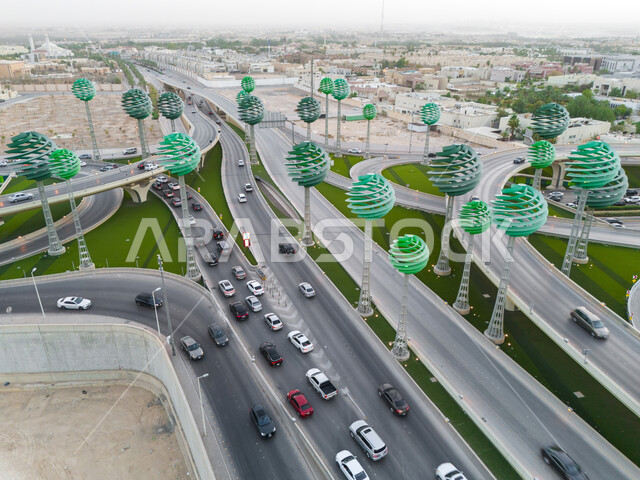 حركة المرور في شوارع وطرقات العاصمة في النهار، الفن الهندسي المعماري للمجسمات الفنية على شكل أشجار خضراء، معالم الرياض المشهورة، دوار عرقة على تقاطع طريق الملك عبد لله مع الملك خالد، تنشيط السياحة في المملكة العربية السعودية