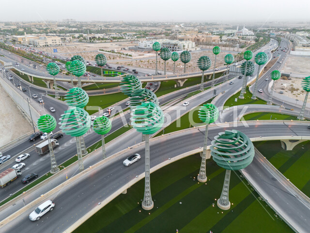 حركة المرور في شوارع وطرقات العاصمة في النهار، الفن الهندسي المعماري للمجسمات الفنية على شكل أشجار خضراء، معالم الرياض المشهورة، دوار عرقة على تقاطع طريق الملك عبد لله مع الملك خالد، تنشيط السياحة في المملكة العربية السعودية