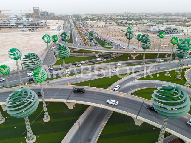 حركة المرور في شوارع وطرقات العاصمة في النهار، الفن الهندسي المعماري للمجسمات الفنية على شكل أشجار خضراء، معالم الرياض المشهورة، دوار عرقة على تقاطع طريق الملك عبد لله مع الملك خالد، تنشيط السياحة في المملكة العربية السعودية