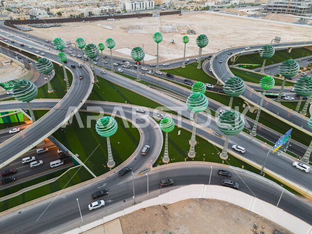 حركة المرور في شوارع وطرقات العاصمة في النهار، الفن الهندسي المعماري للمجسمات الفنية على شكل أشجار خضراء، معالم الرياض المشهورة، دوار عرقة على تقاطع طريق الملك عبد لله مع الملك خالد، تنشيط السياحة في المملكة العربية السعودية