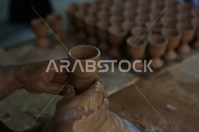 حرف وصناعات يدوية شعبية من التراث السعودي العريق، العمل في صناعة الخزفيات, اواني خزفية مصنوعة من الطين، صنع الجرار الفخارية المزخرفة، صورة مقربة لايدي رجل عربي سعودي خليجي يقوم بصناعة الفخار