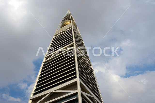 النمو والتطور العمراني في العاصمة، صورة من الأسفل لبرج الفيصلية في مدينة الرياض، الفن الهندسي المعماري للأبراج وناطحات السحاب في المملكة العربية السعودية، معالم ومباني مشهورة، منظر السماء المليئة بالغيوم البيضاء