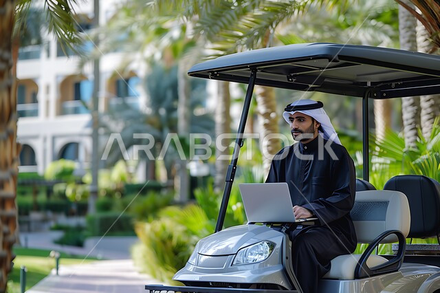 الاستمتاع بالاجواء الصيفيه أثناء انجاز المهام اليومية, رجل عربي خليجي سعودي يرتدي الزي التقليدي يجلس في عربة الغولف الكهربائية يستخدم جهاز الحاسوب المحمول, مفهوم العمل المتنقل في الهواء الطلق, دمج التقنيات الحديثة المتطورة في الحياة العملية