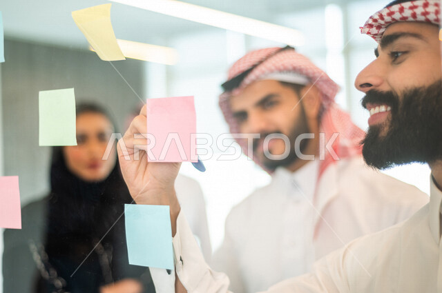 رجل عربي خليجي سعودي يدون الملاحظات والمهام على الورق ، فريق عمل خليجي سعودي يتشارك بتحديد الاهداف ، اجتماع داخل شركة سعودية ، انجاز مهام العمل ، تحقيق اهداف الشركة ، تطوير العمل