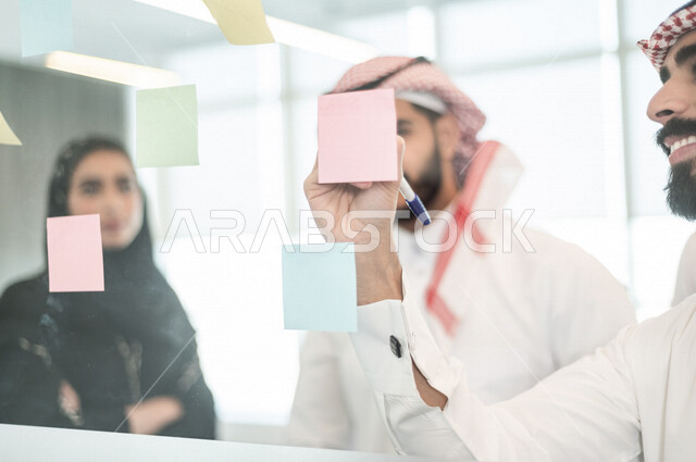 رجل عربي خليجي سعودي يدون الملاحظات والمهام على الورق ، فريق عمل خليجي سعودي يتشارك بتحديد الاهداف ، اجتماع داخل شركة سعودية ، انجاز مهام العمل ، تحقيق اهداف الشركة ، تطوير العمل